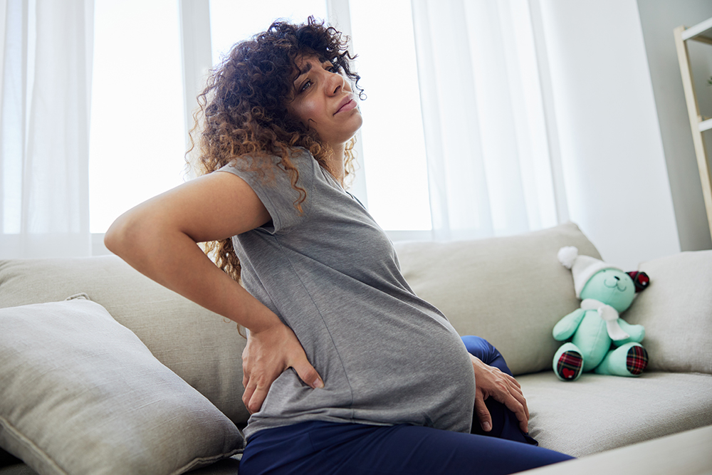 5 PT techniques that can improve SI joint pain while pregnant pregnant woman sitting on the couch lower back pai 2023 12 19 07 01 11 utc 1 5 pt techniques that can improve si joint pain while pregnant hip pain